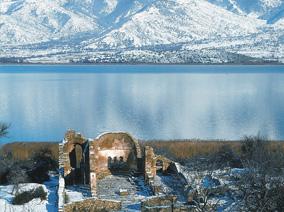Remains of an ancient building with a lake and snow-capped mountains in the background