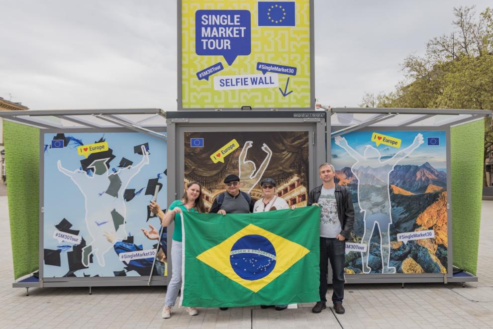 Four people showing Brazilian flag in front of the Tour booth