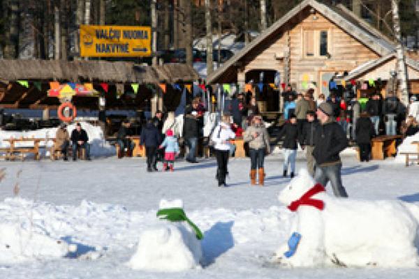 Snowmen and people in the background with a mountain hut