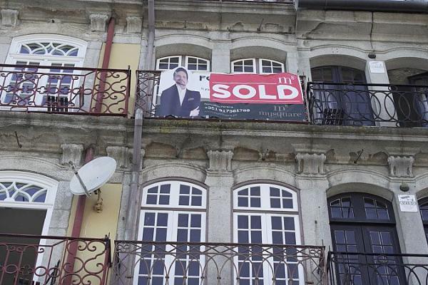 Video still of Porto city classic multistory buildings from the early 1900s with realtor sign hanging from one balcony with the message "sold".