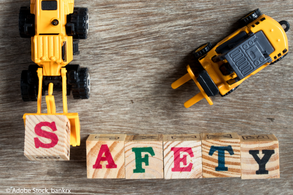 A toy digger and forklift move wooden blocks with painted letters on them to form the word "safety".