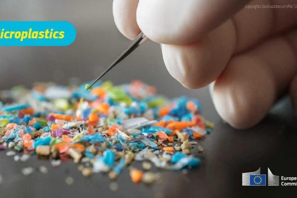 A photograph of a hand picking up tiny pieces of plastic with a pincer